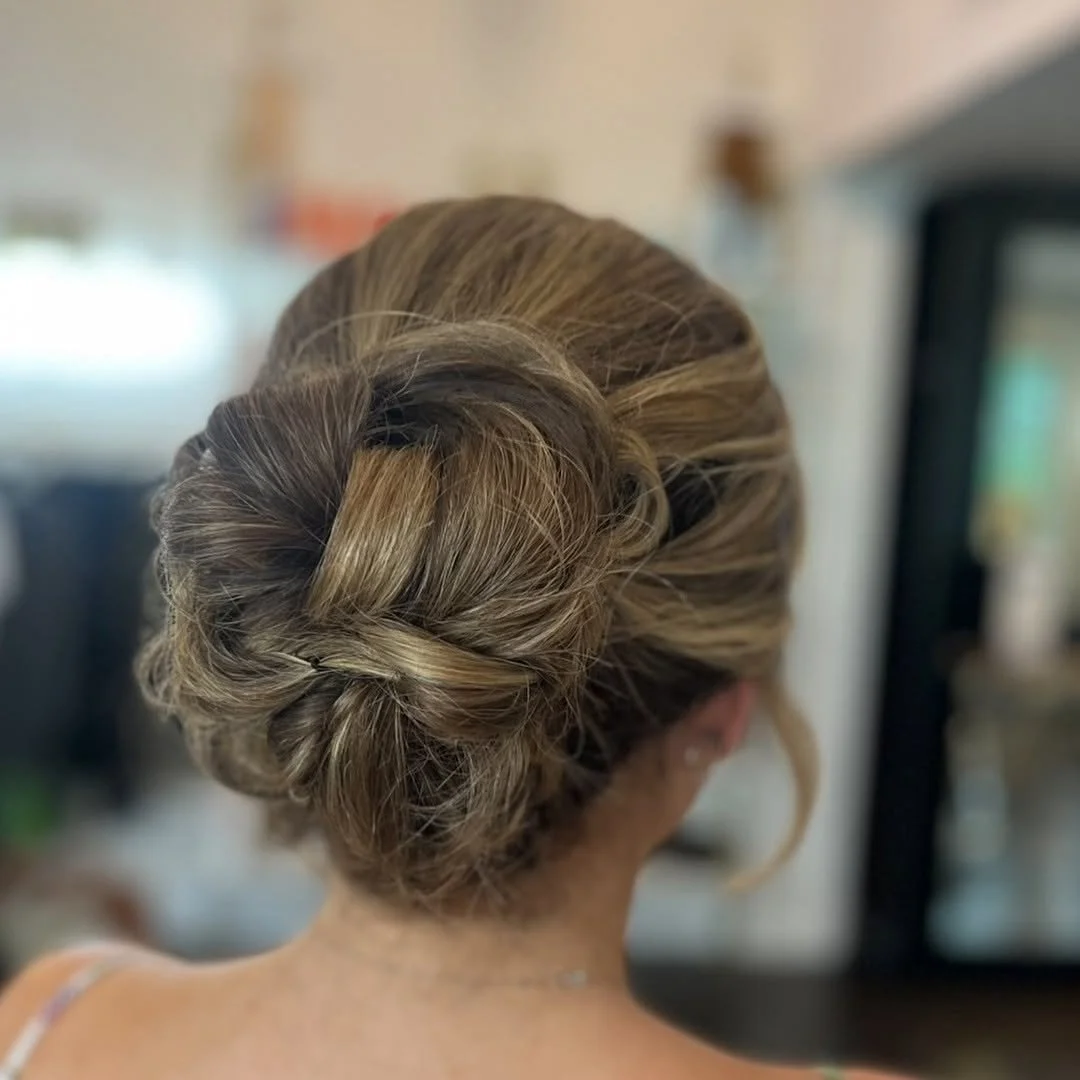  Elegant low bridal bun with soft texture and dimensional blonde tones, styled by TEAL Hair &amp; Makeup Studio. 