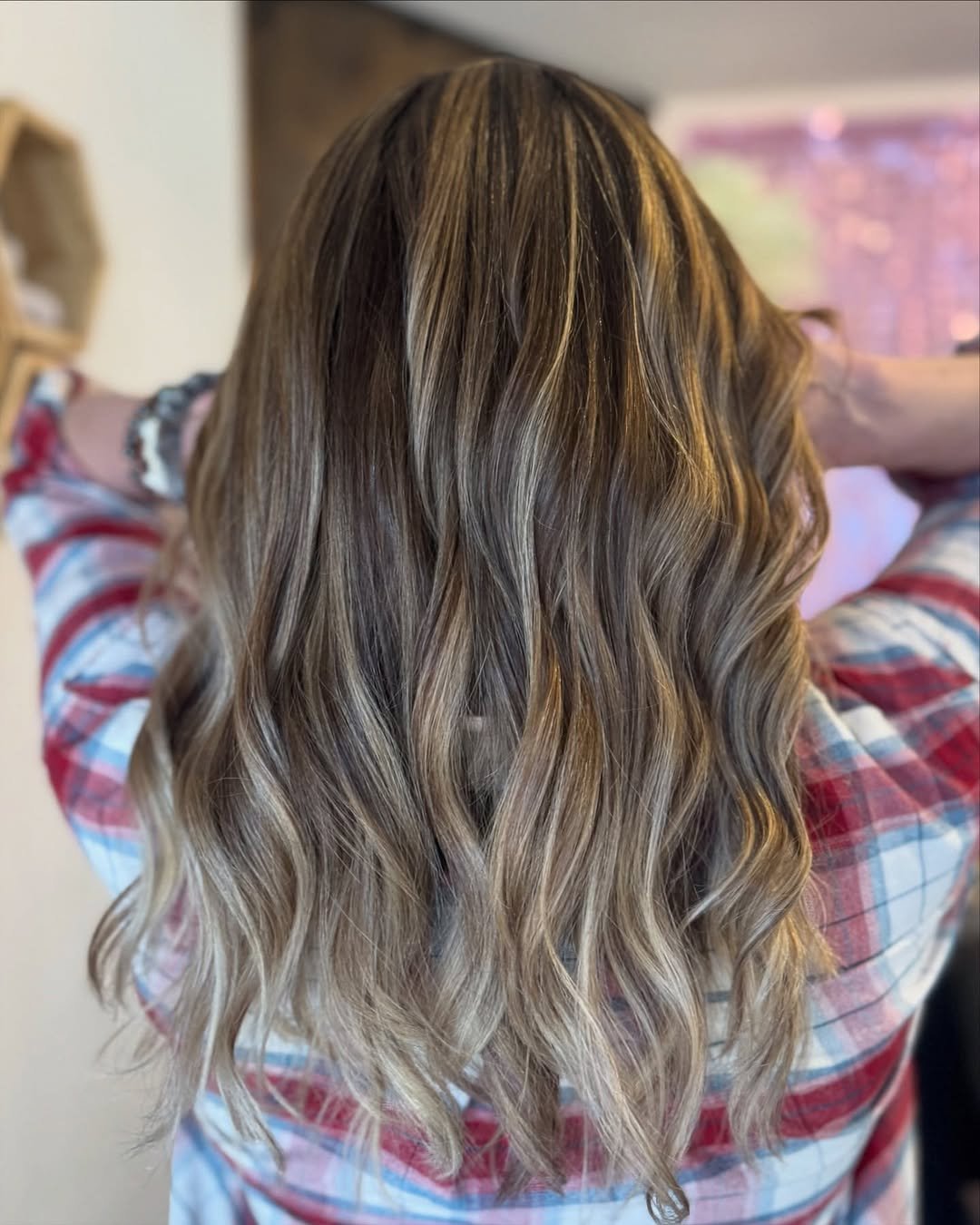  Back view of medium-length wavy hair with dimensional balayage highlights in caramel and ash blonde tones, styled by Teal Hair and Makeup Studio. 