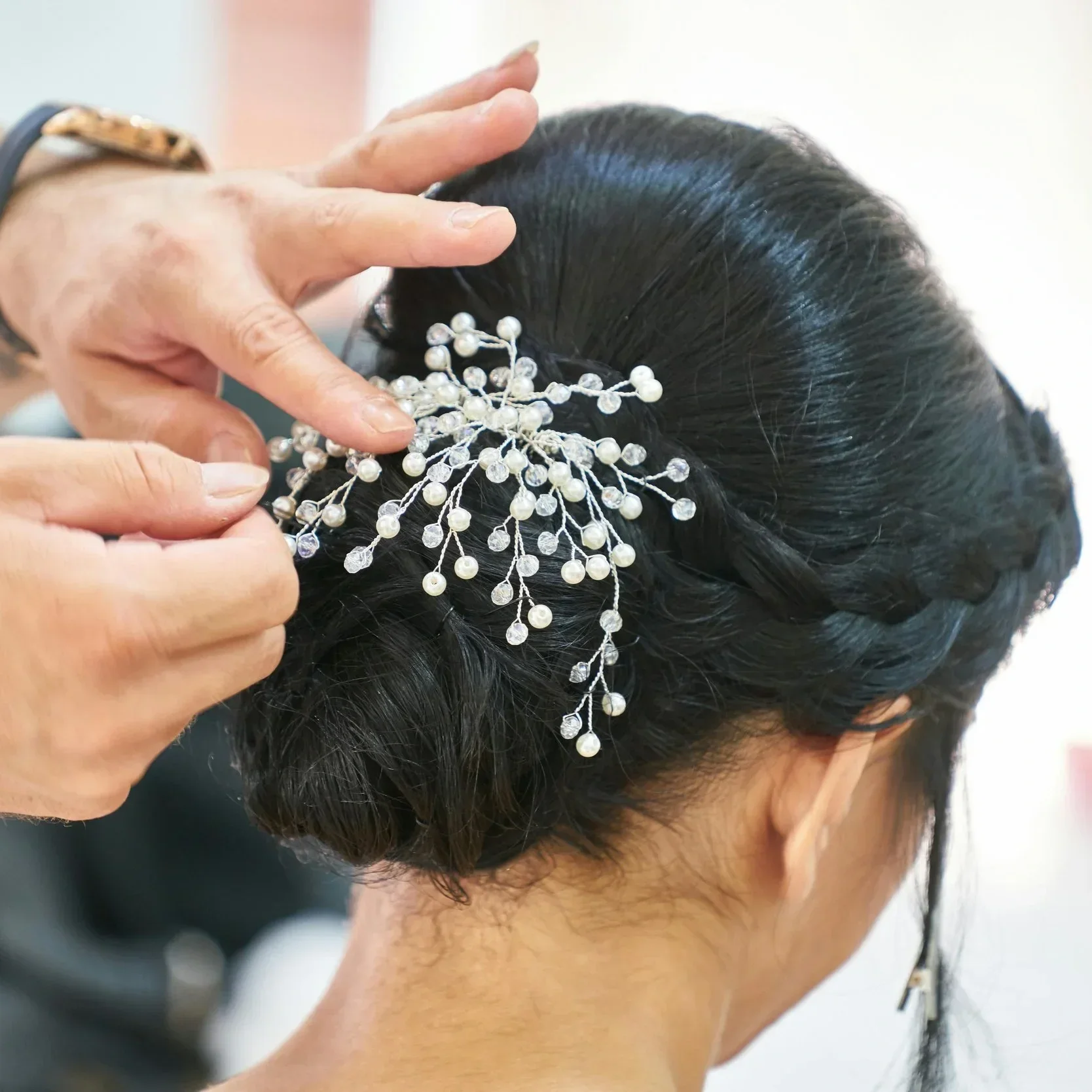 Stylist securing a pearl and crystal hair accessory into an elegant dark bridal updo