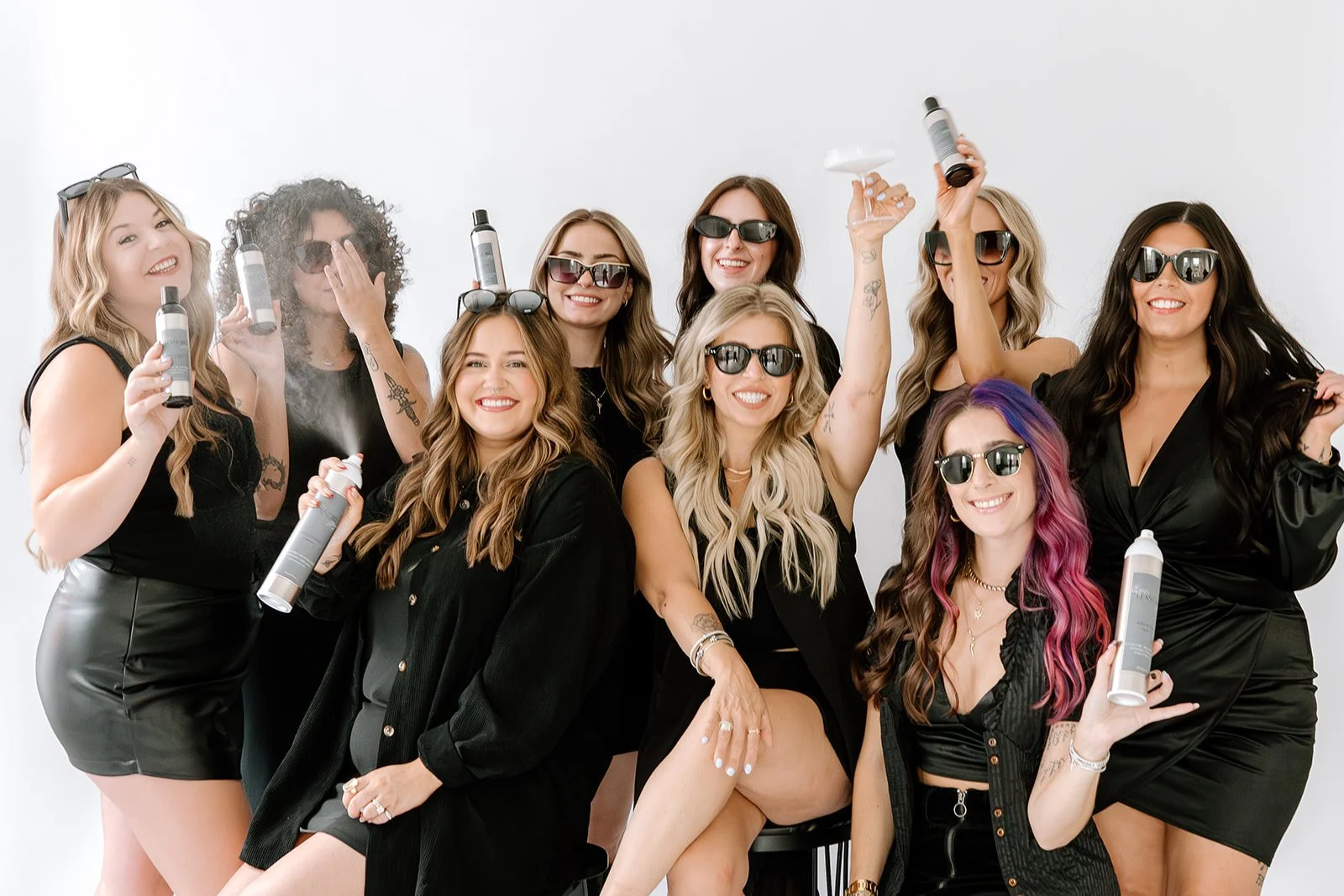 Teal Studio team posing together in black outfits and sunglasses while holding professional hair products