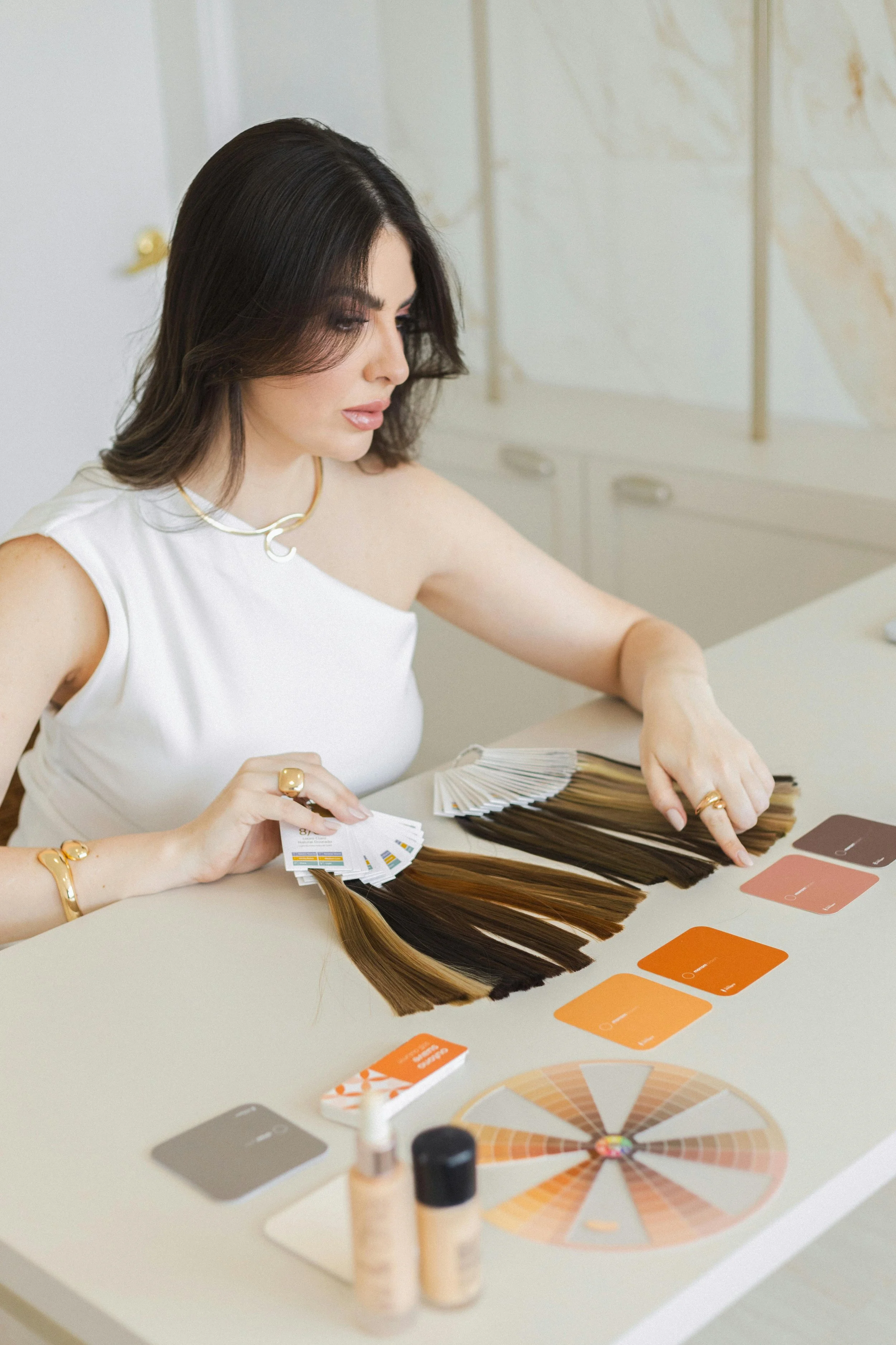 A woman reviews hair color swatches and warm-toned color cards on a table, comparing shades to select the most flattering tones.