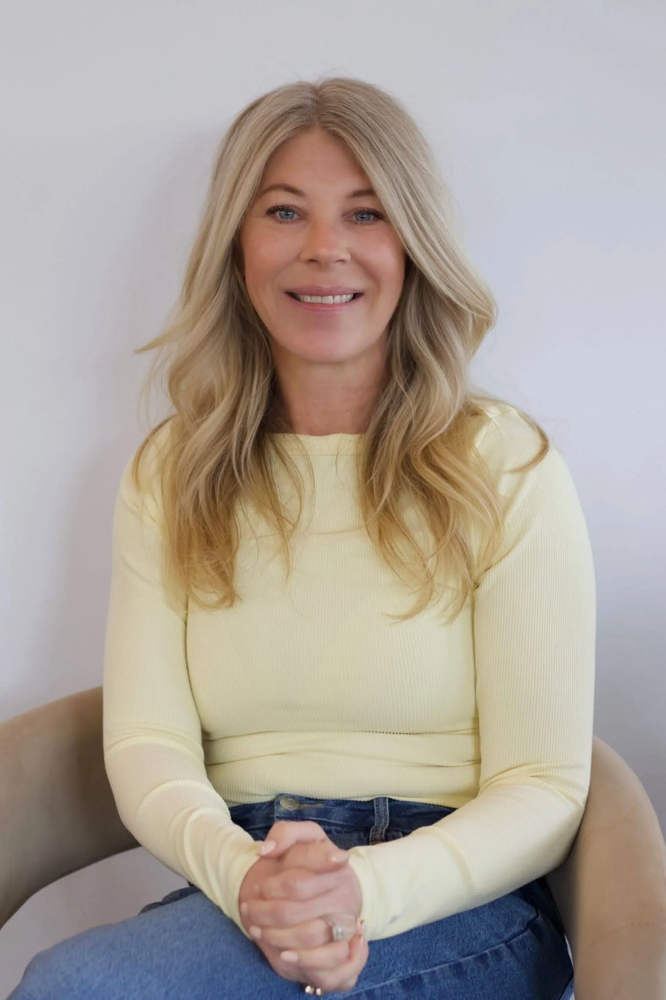 Jess Bradley, Teal Studio salon manager, smiling while seated with long wavy blonde hair and a light yellow top