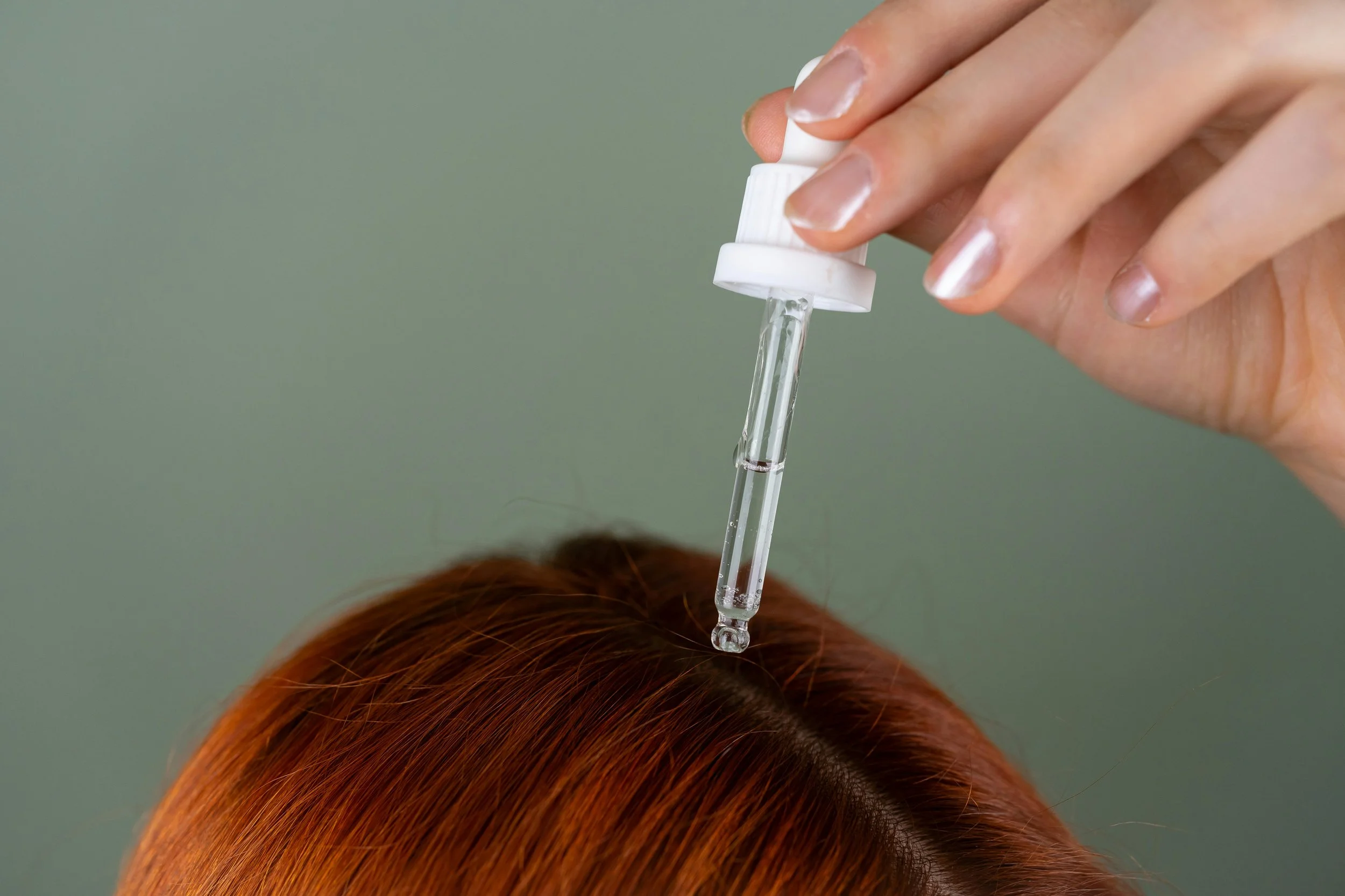 Dropper applying scalp serum to the part of red hair to support scalp hydration and hair health.