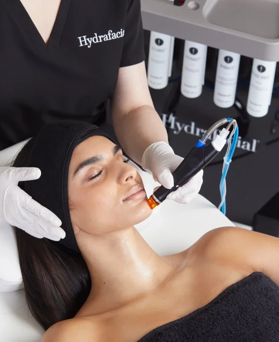 A client relaxes during a Hydrafacial treatment, as a skincare professional uses advanced technology to deeply cleanse and hydrate the skin.