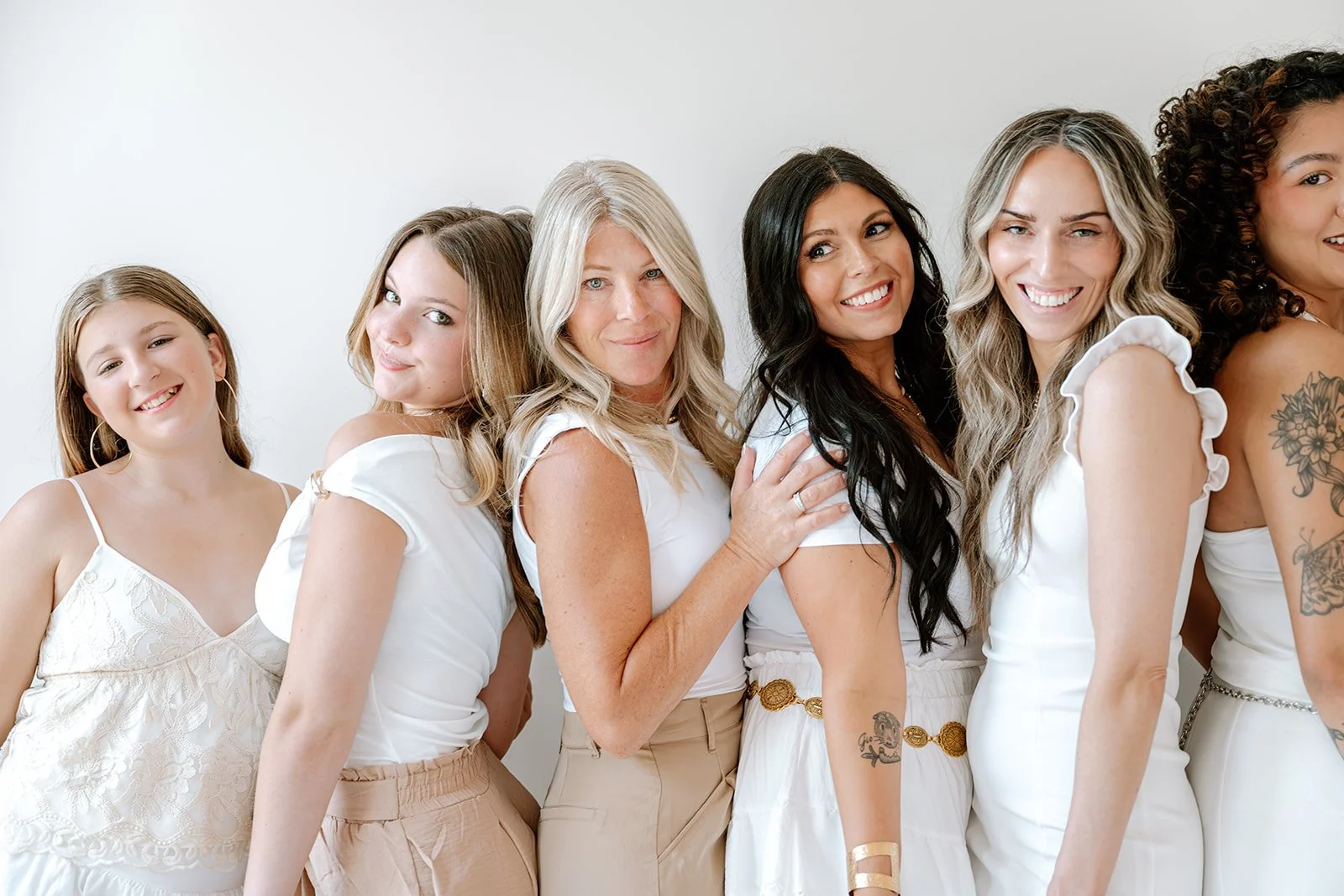 Six smiling women posing together in a bright salon setting, showcasing a variety of hair colors, lengths, and textures, from blonde waves to dark curls.