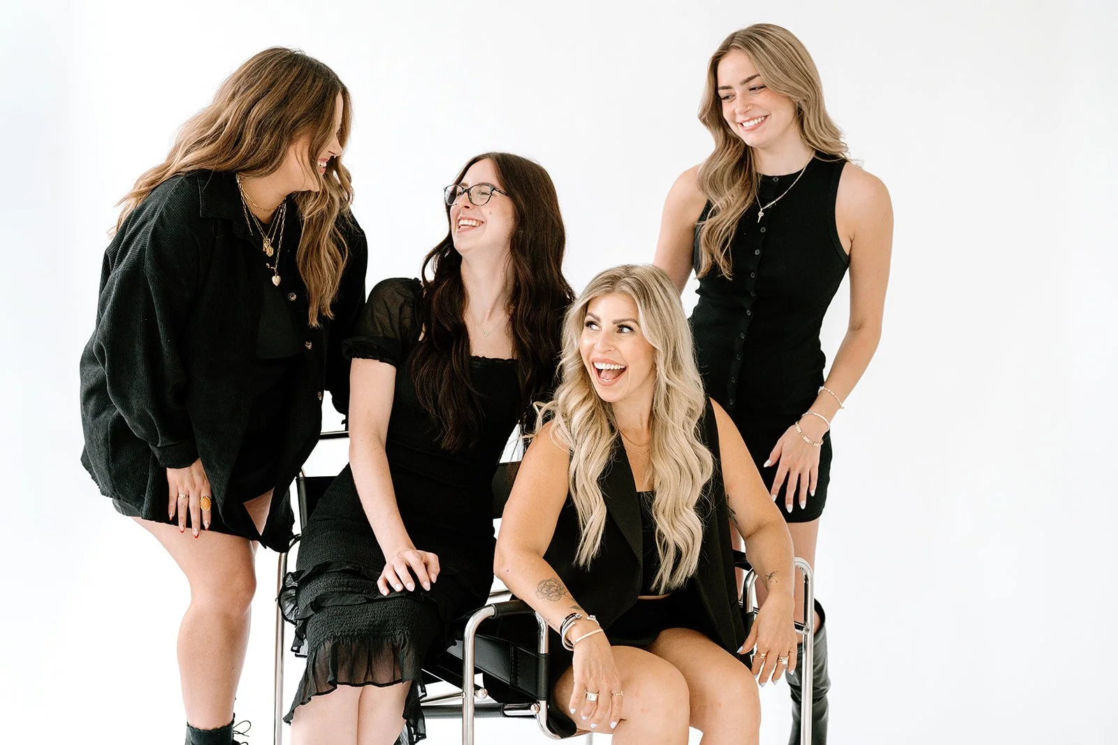 Four Teal Studio team members in black outfits smiling and laughing together against a white studio background.