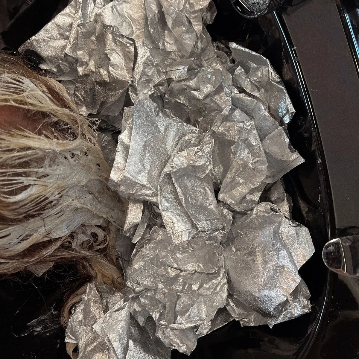 Crumpled silver hair foils surround partially lightened hair during a coloring process at a salon sink.