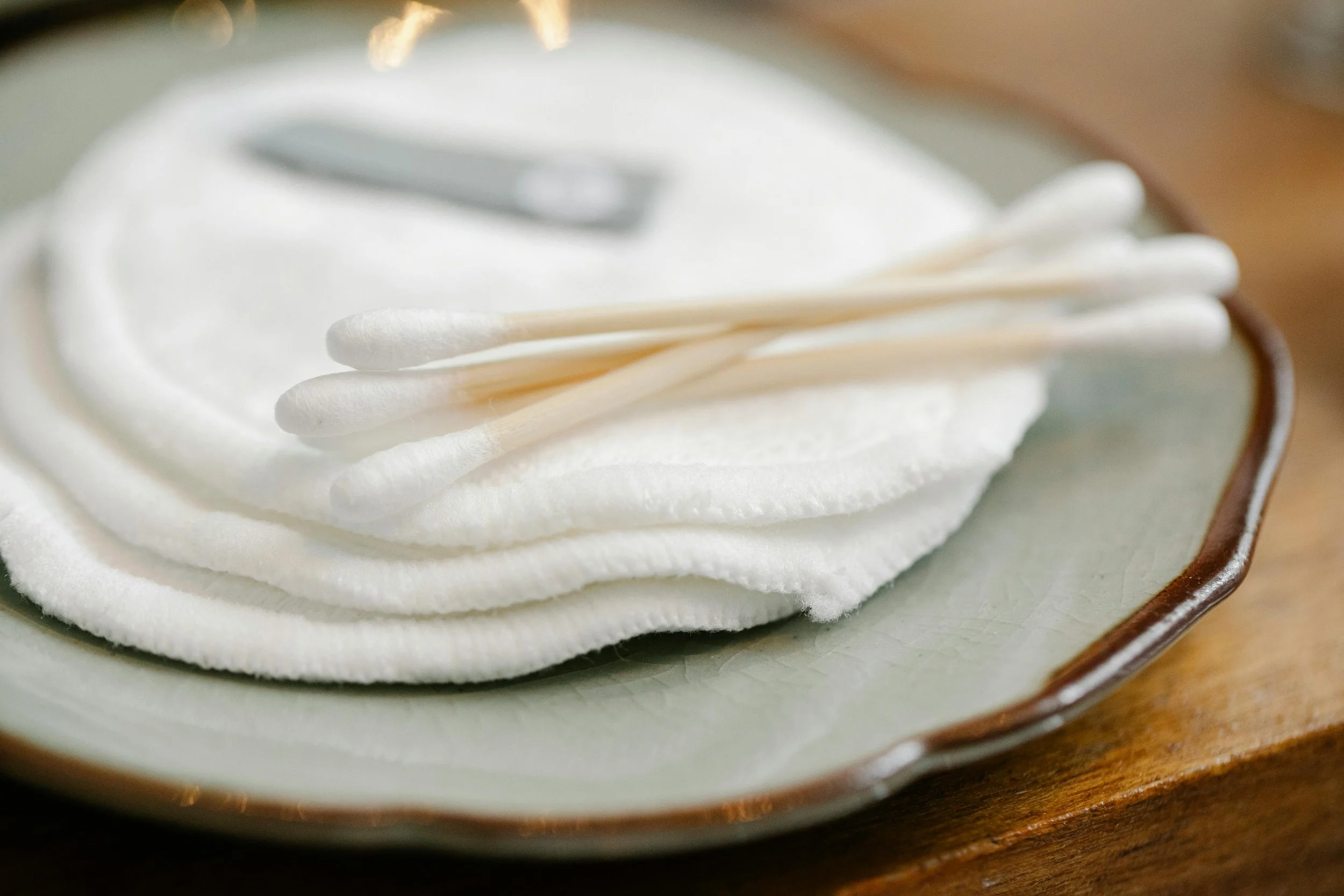 A stack of disposable cotton pads and cotton swabs rests on a small plate, representing single-use items commonly used in a salon.