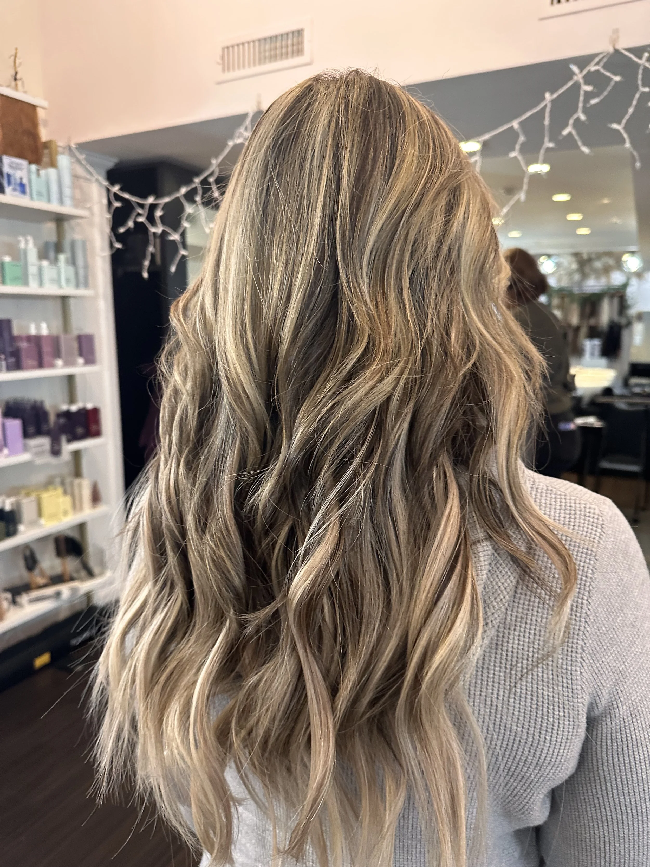 Back view of long, voluminous blonde hair extensions featuring seamlessly blended ash blonde and honey highlights, soft waves, and natural-looking dimension, showcasing professional hair extensions at TEAL Hair & Makeup Studio.
