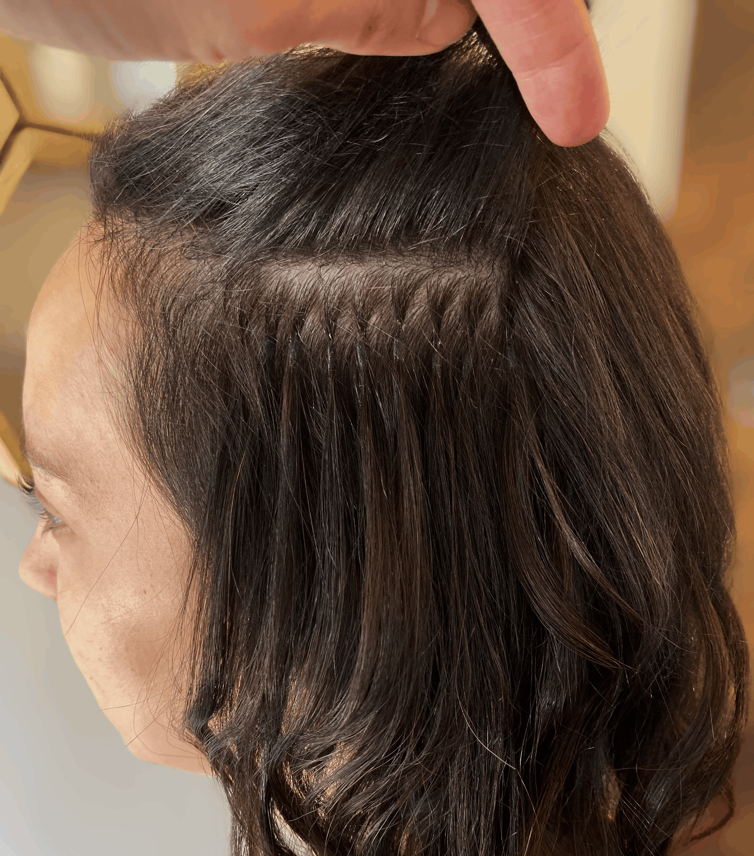 Close-up of K-tip hair extensions installed on fine, dark brunette hair, showing discreet keratin bond attachments near the roots for added length and volume, highlighting hair extension solutions from TEAL Hair & Makeup Studio.