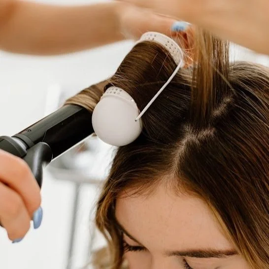 Stylist blow-drying brown hair with a round brush during a professional wash and blowout.