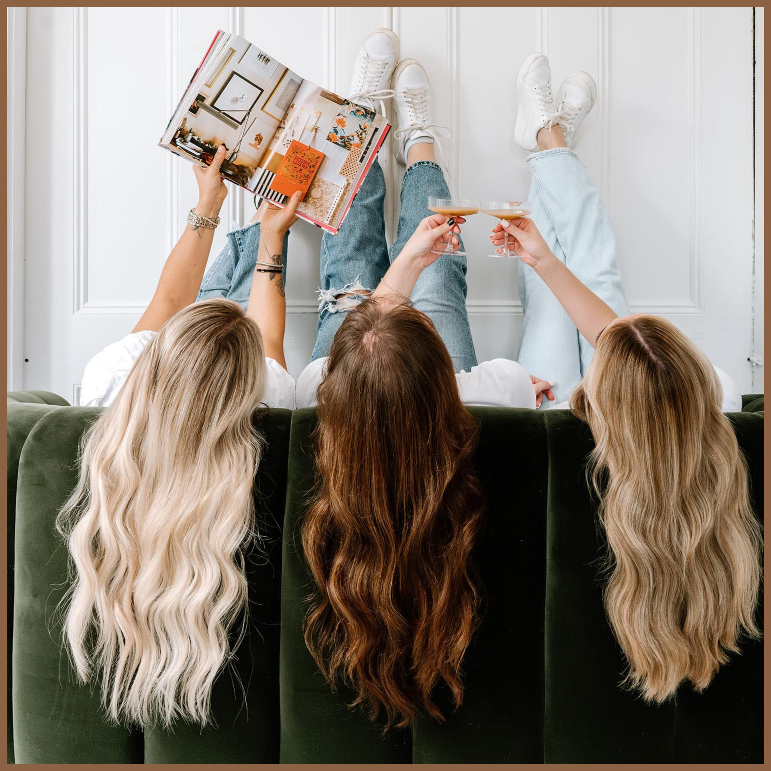Three women with long blonde and brunette wavy hair seated on a green sofa, holding drinks and an open magazine.