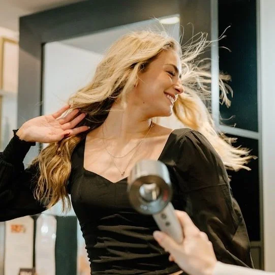 Stylist blow-drying long blonde hair for a smooth, voluminous finish at Teal Studio.