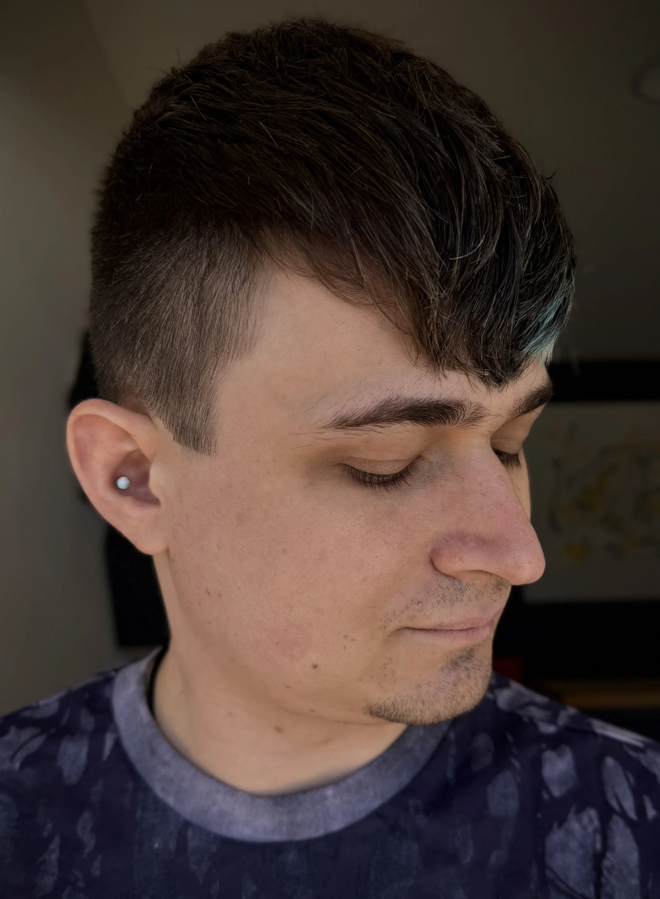 Side-profile of a person with a textured short haircut featuring subtle teal tones, clean faded sides, and natural makeup, showcasing precision clipper and scissor work at Teal Hair and Makeup Studio.