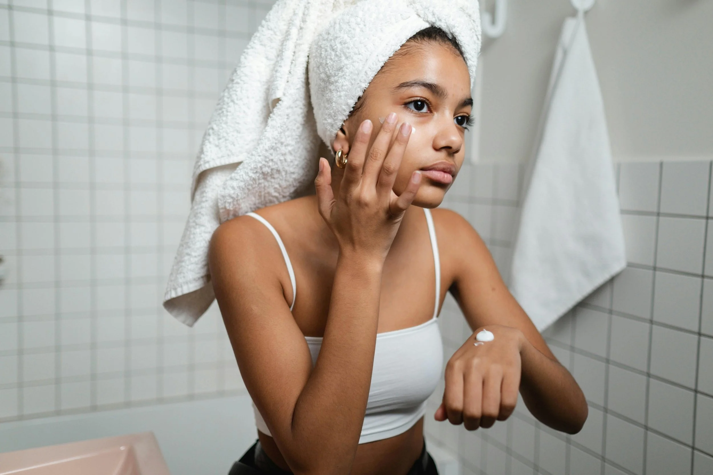 A woman applies skincare in her bathroom mirror, representing the early stages of building a consistent skincare routine months before a wedding day.