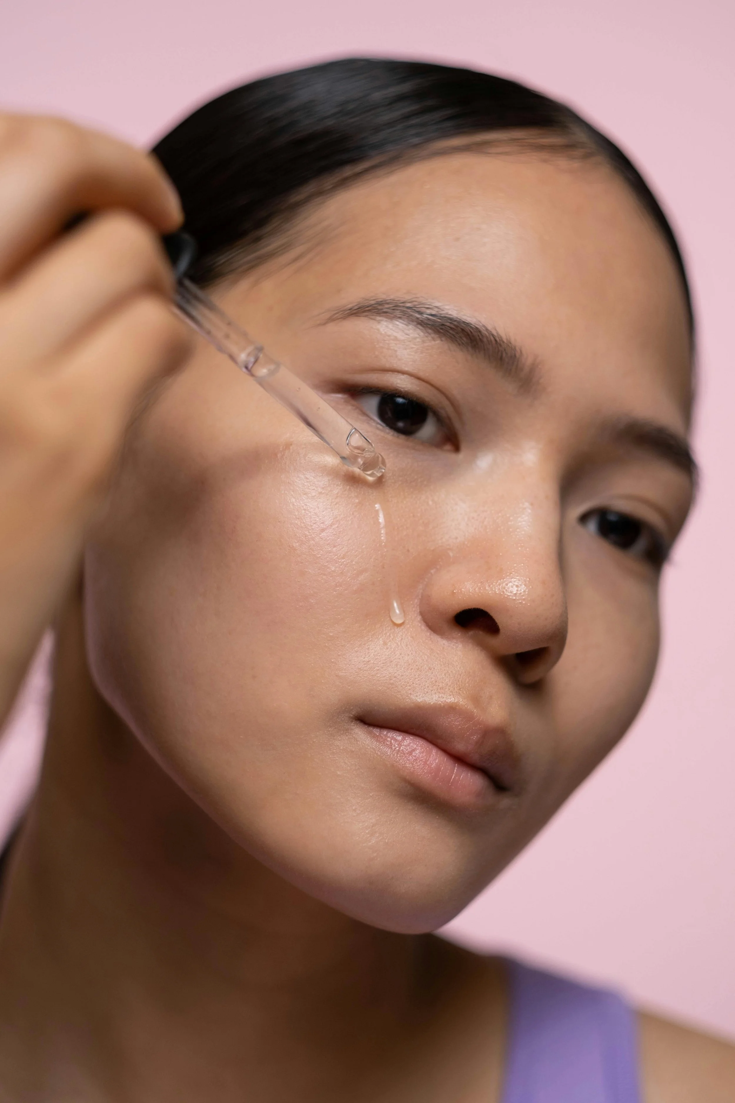 A woman applies a hydrating facial serum with a dropper for a dewy, moisturized glow.