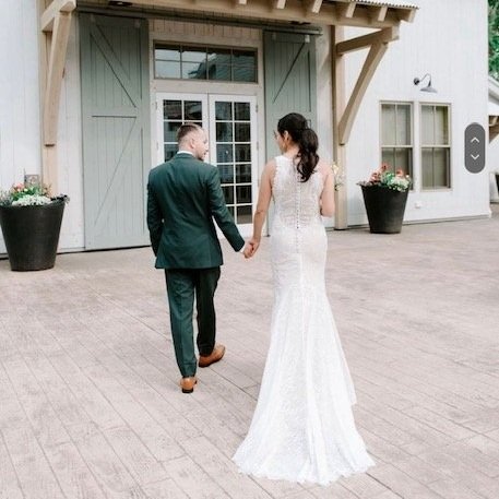 Bride with formal ponytail hairstyle walking hand in hand with groom outside a wedding venue.