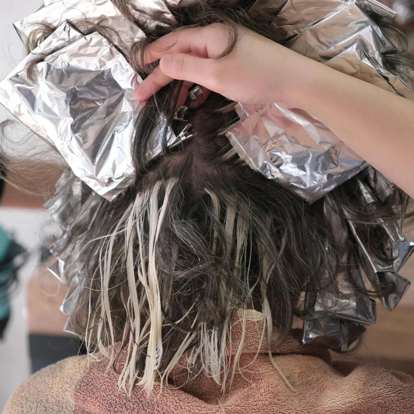 Hair colorist applying dimensional highlights with foils during a salon color service