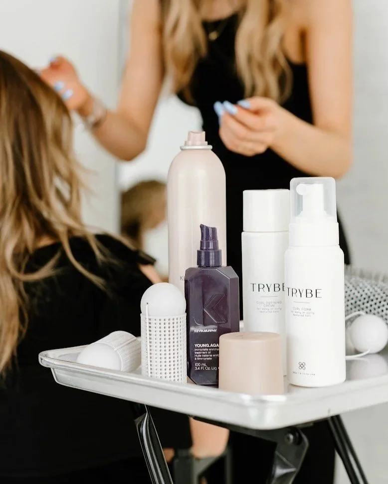 Deep conditioning and scalp treatment products on a salon cart beside a client receiving hair care