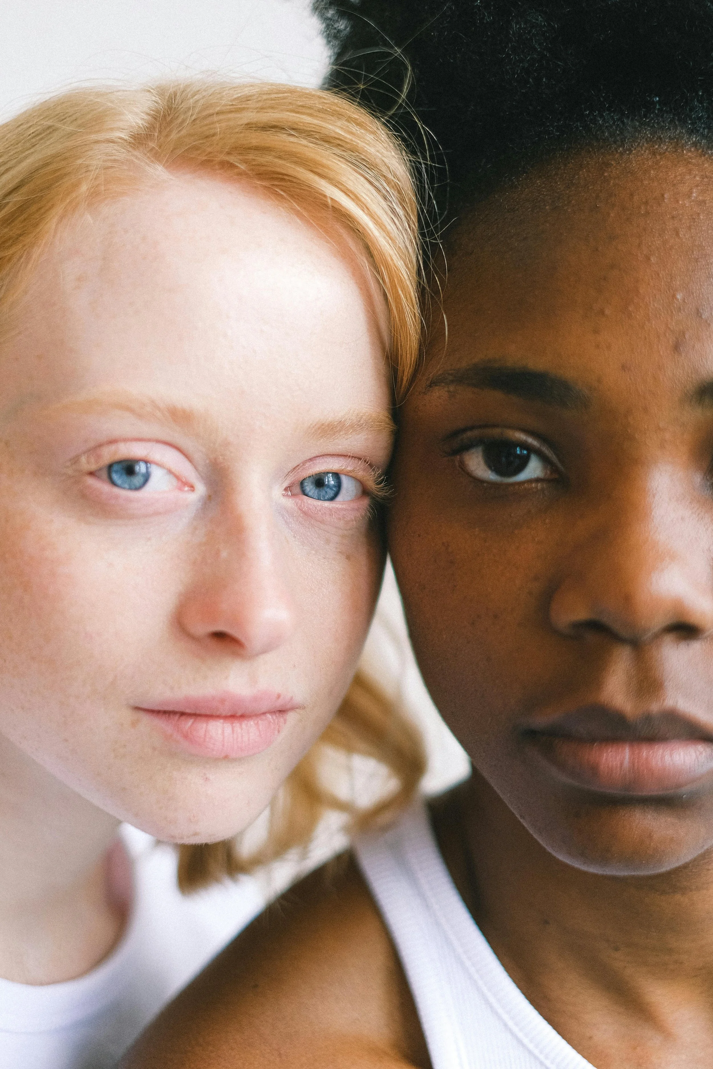 Two women pose closely together, highlighting their striking eyes and natural beauty.