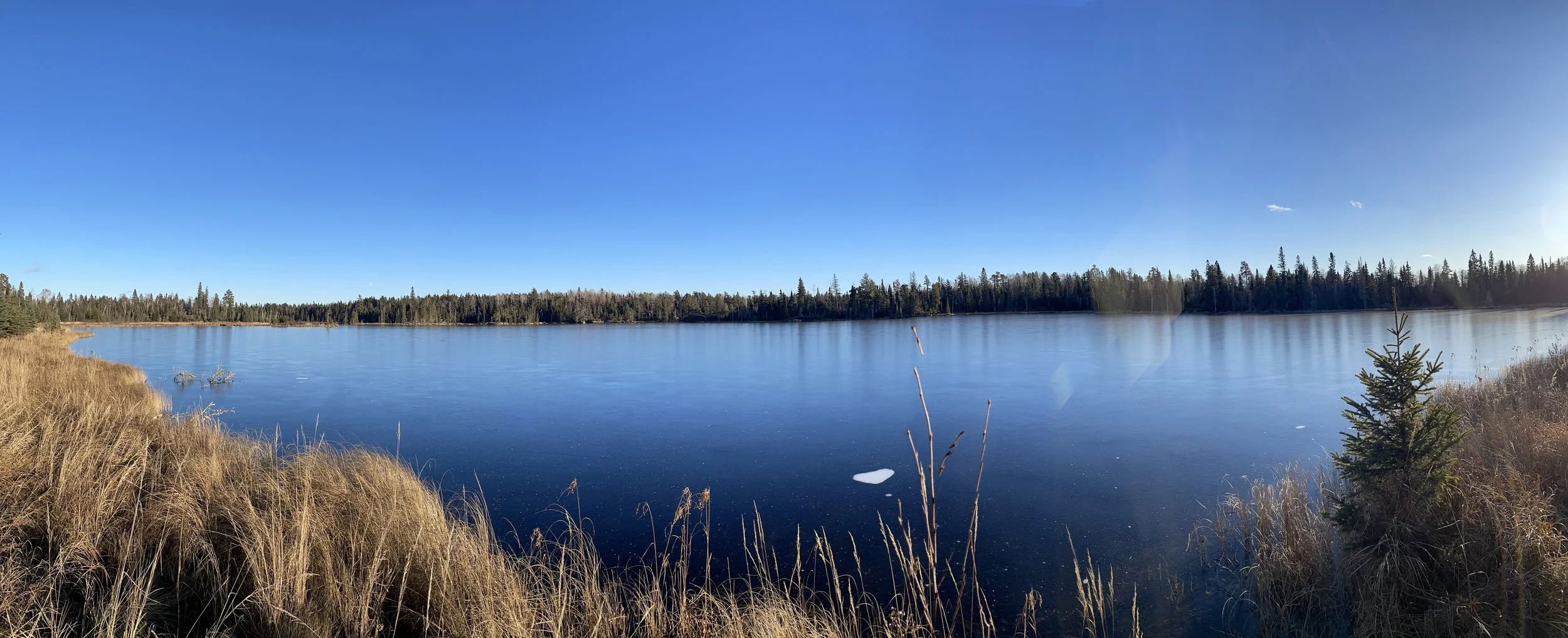 Panoramic view of frozen clear ice lake under blue sky in Ely MN, BWCA area, November 24 2023. Arrowhead Outdoors Ely MN winter fishing report with ice house rentals, tackle, hunting gear & camping supplies.
