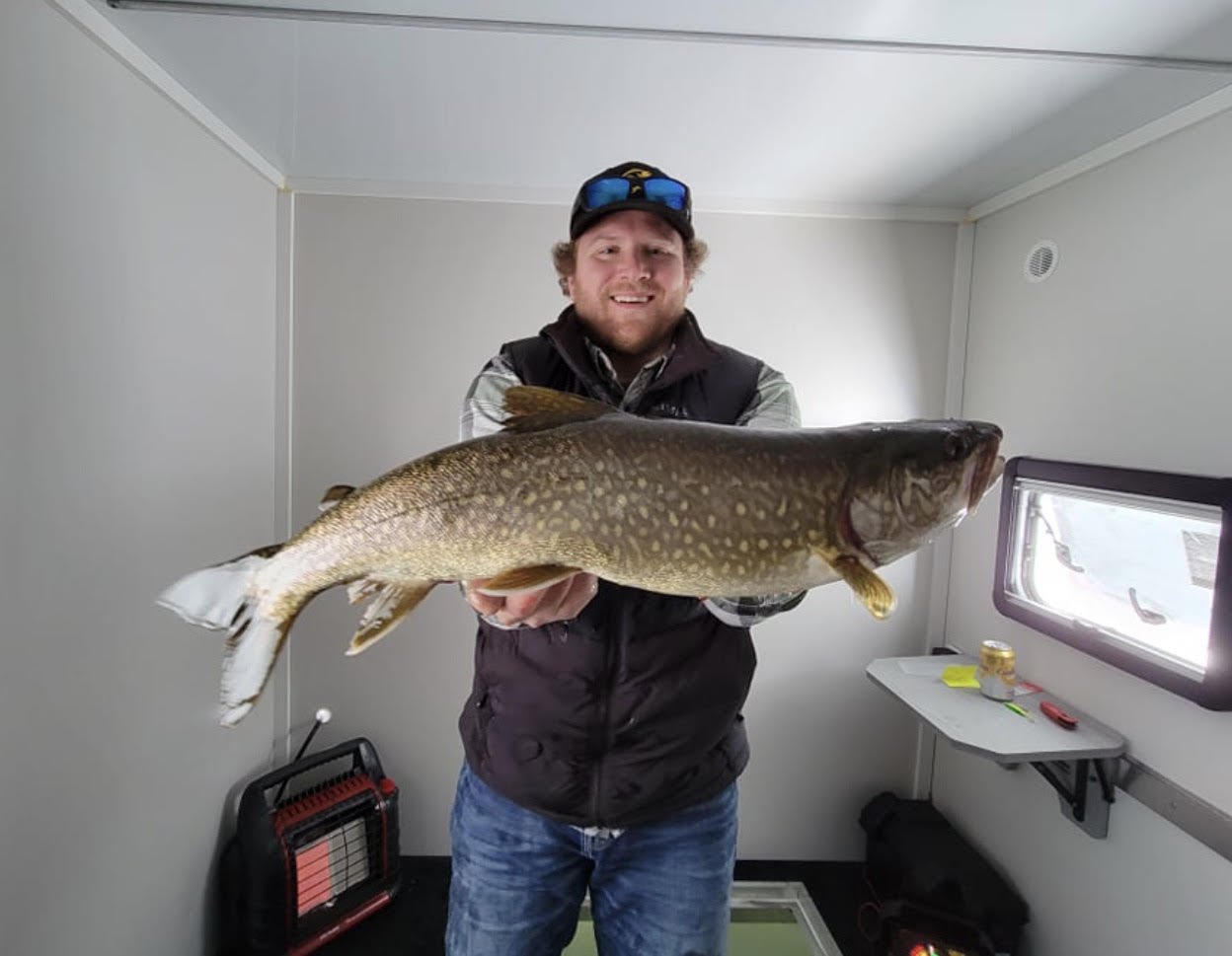 Angler holds big lake trout inside Arrowhead Outdoors ice house rental February 12, 2025 in Ely MN BWCA. Winter fishing report.