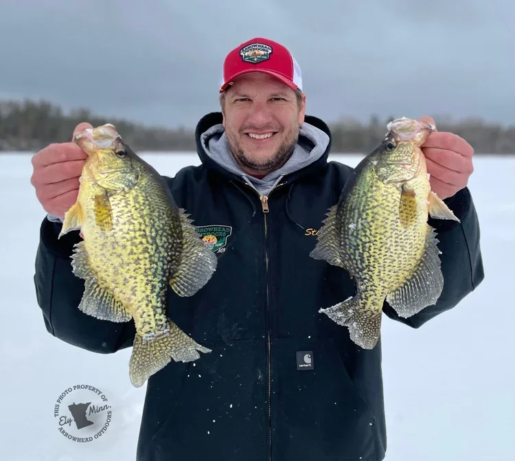 Angler holding crappie on thick ice Ely MN BWCA from Arrowhead Outdoors April 20 2022 fishing report 27-37 inch ice snow cover 20 ft edges deeper holes tungsten jigs soft plastics waxies minnows snowy Northwoods late winter scene