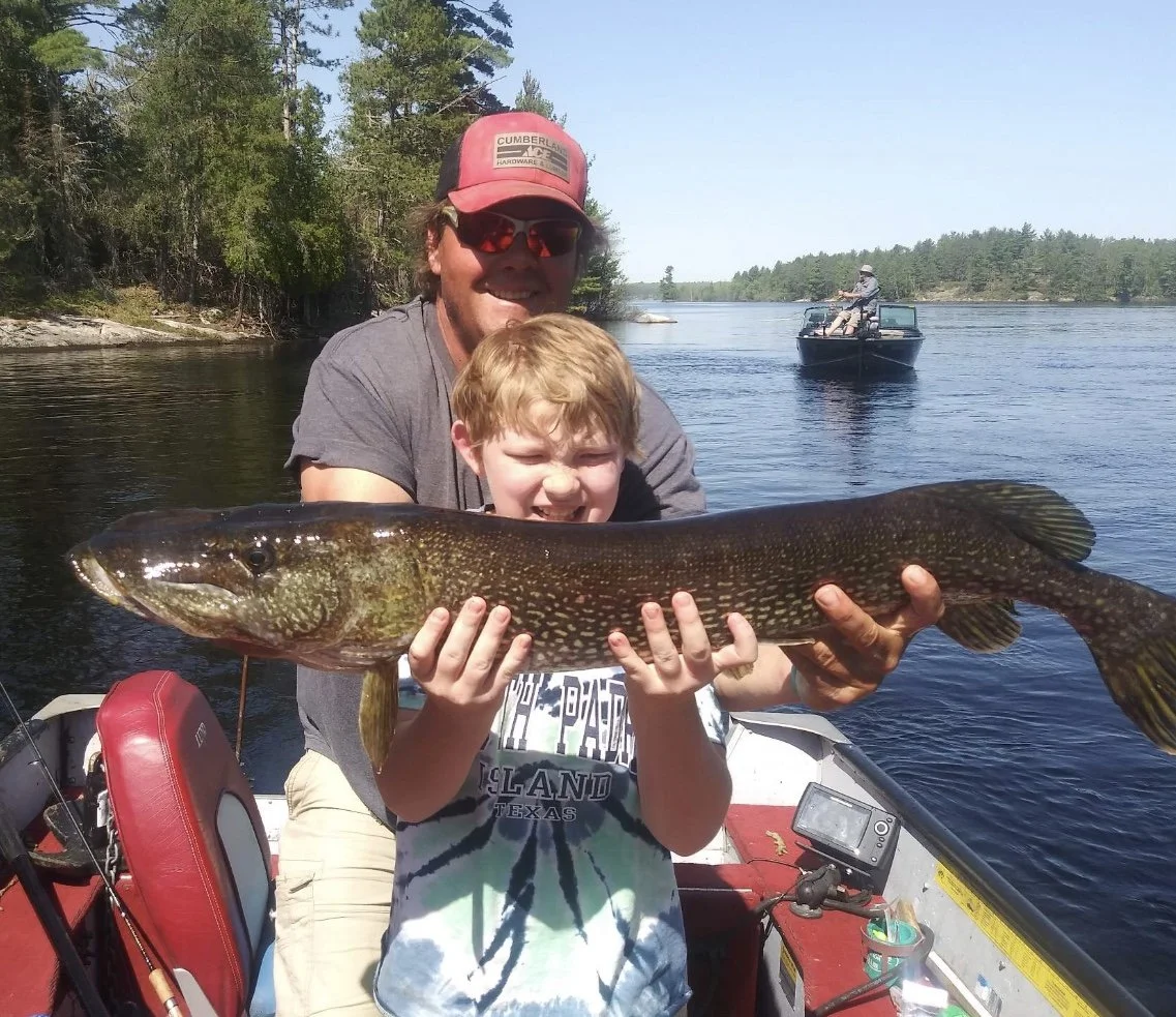 Ely MN BWCA northern pike catch in Arrowhead Outdoors fishing report June 27 2023 – father-son duo holding long spotted pike on boat sunny lake