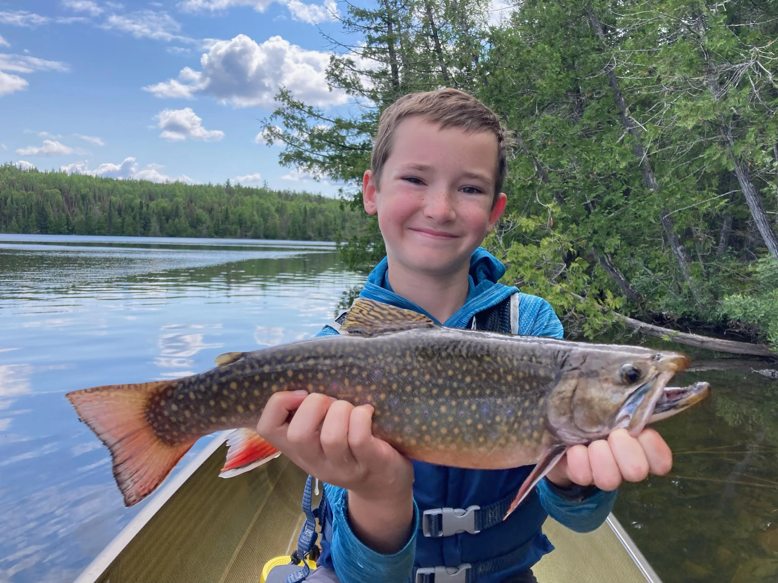 Young angler holds trophy brook trout caught on white twister in canoe Ely MN, BWCA area, July 23 2024. Arrowhead Outdoors Ely MN fishing report with premium tackle, hunting gear & camping supplies available.