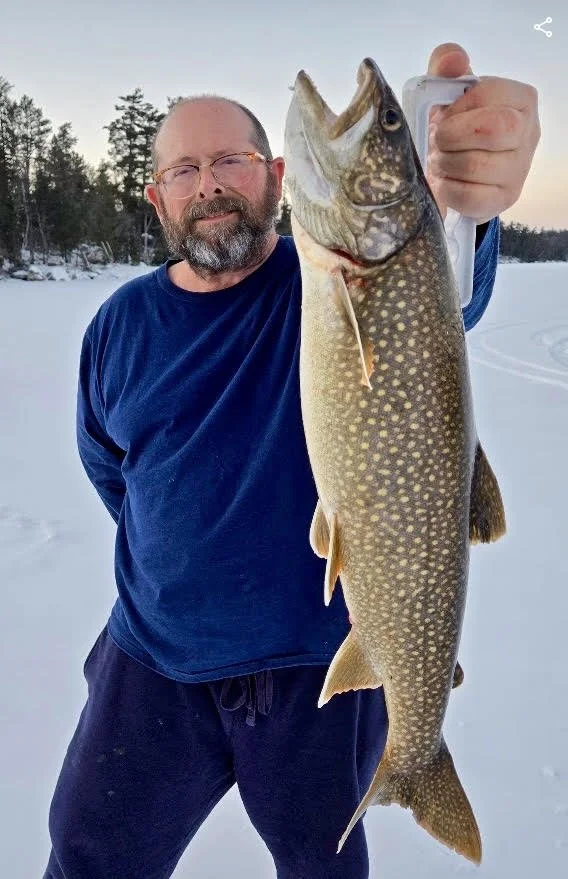 Angler holds lake trout caught on pike sucker at sunset February 19, 2025 on ice in Ely MN BWCA. Winter fishing report from Arrowhead Outdoors.