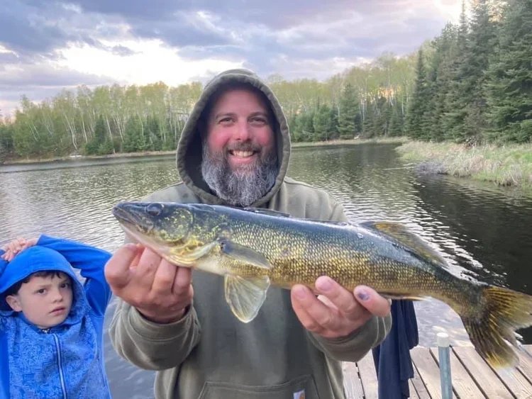 Ely MN BWCA walleye open water family catch July 13 2021, dad holding golden walleye at dusk with son watching on boat, Arrowhead Outdoors report