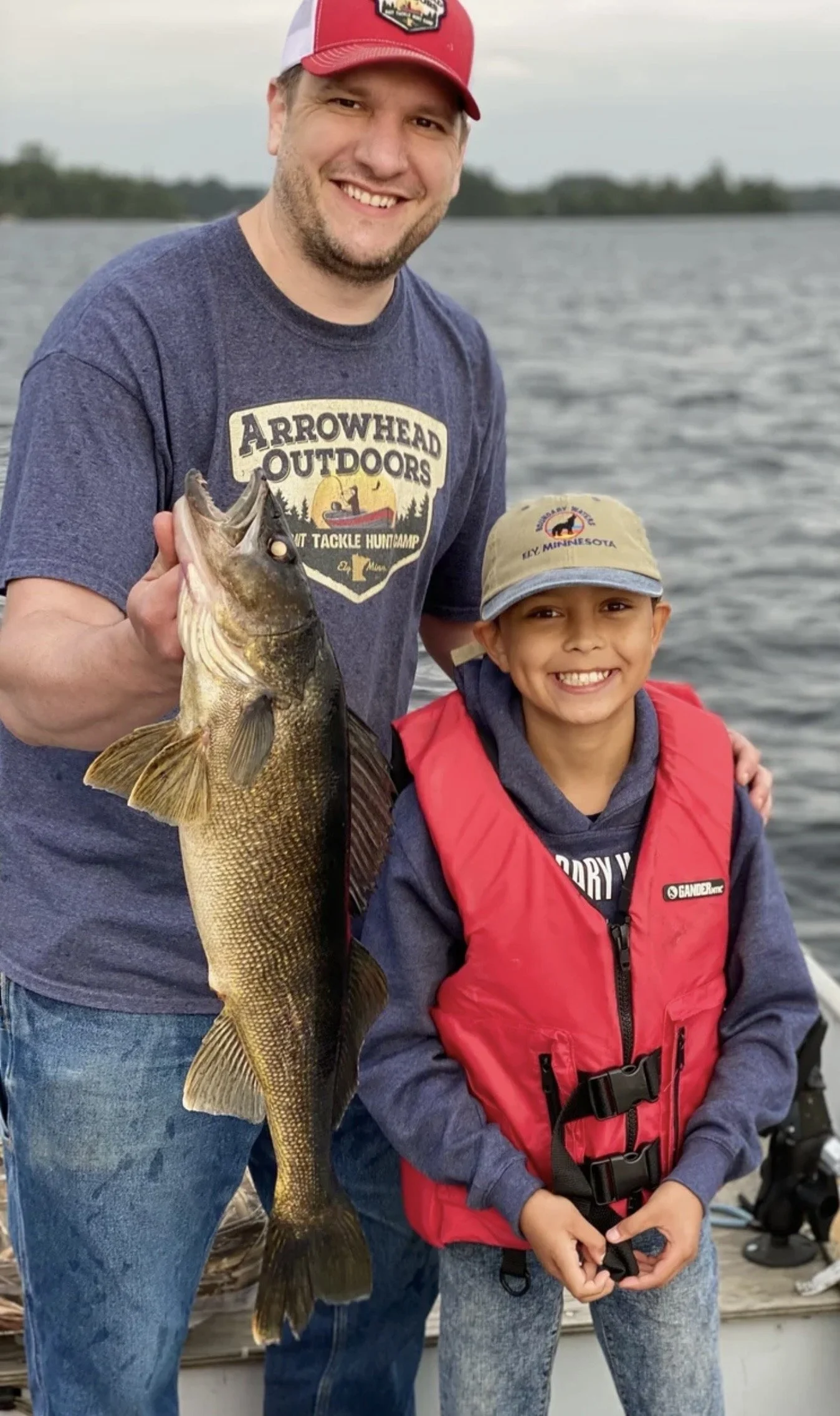 Ely MN BWCA walleye open water family catch July 21 2021, dad holding golden walleye at dusk with son smiling on boat, Arrowhead Outdoors report