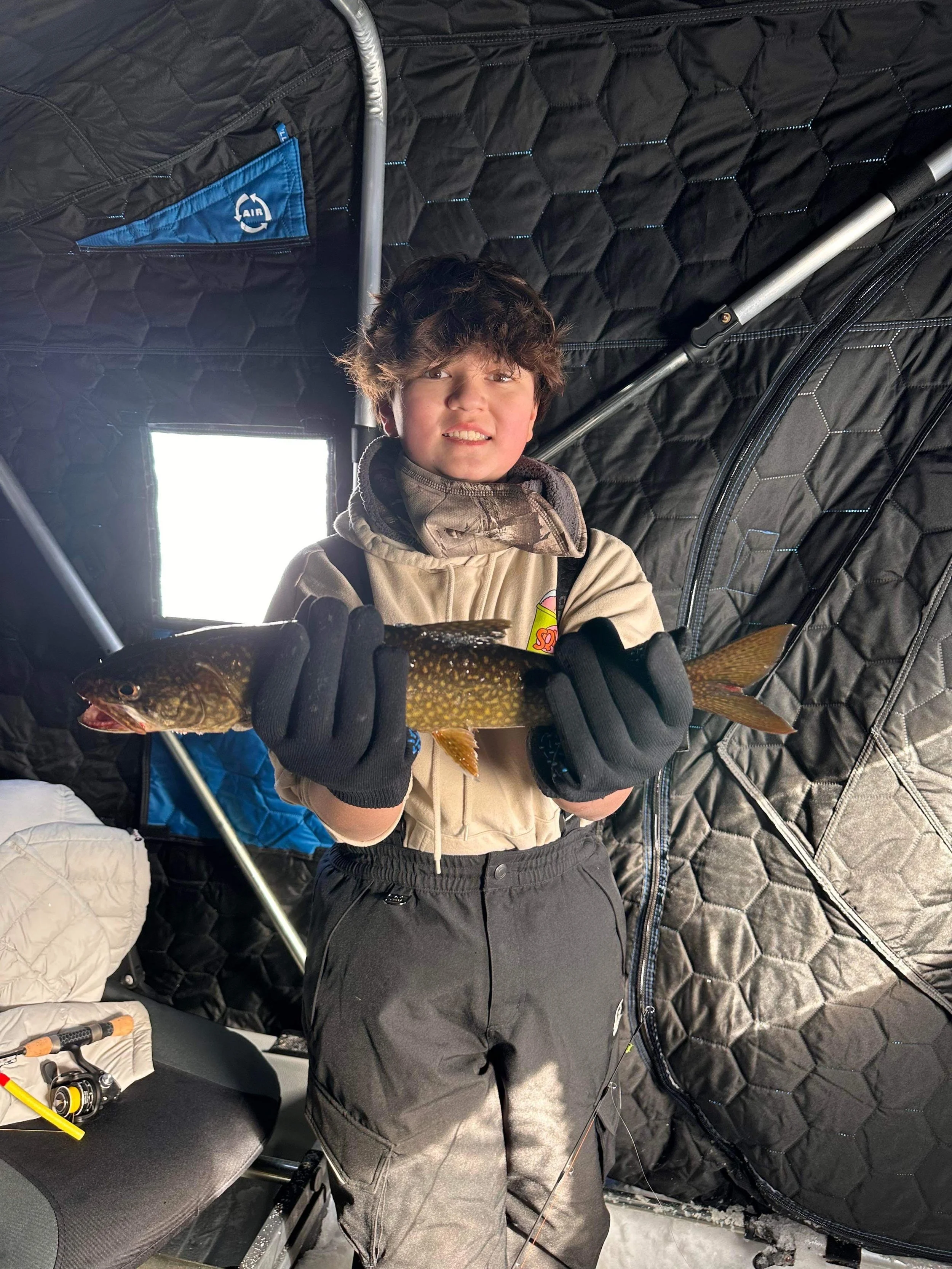 Ely MN BWCA lake trout catch in Arrowhead Outdoors fishing report February 28 2023 – young angler inside heated ice house holding vibrant lake trout
