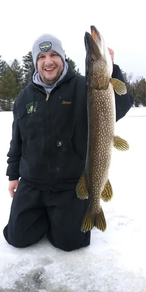 Ely MN BWCA northern pike ice fishing catch Feb 23 2021, Steve kneeling with big toothy pike on snowy frozen lake, Arrowhead Outdoors report