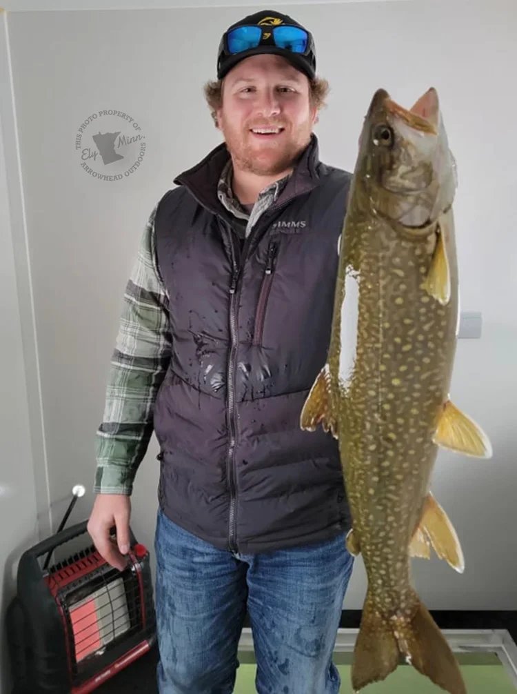 Angler holding lake trout on ice Ely MN BWCA from Arrowhead Outdoors March 2 2022 fishing report up and down action deeper water productive bucktails tubes red white blue pink snowy Northwoods scene stream trout early wax worms eelpout night