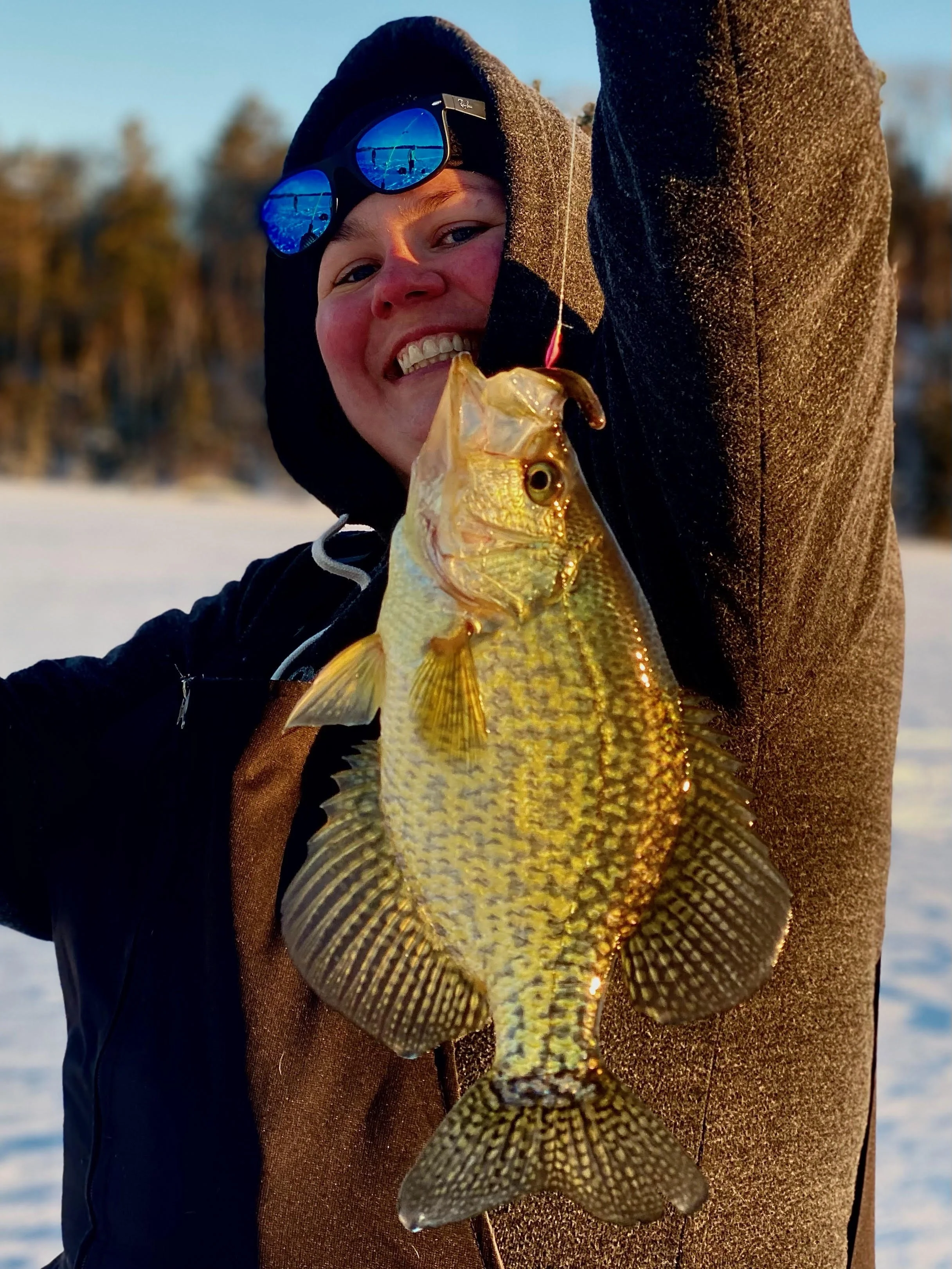 Smiling angler raises fat slab crappie caught on pink/red jig with white tail at sunset March 12, 2025 near Ely MN BWCA. Classic late-ice panfish thrill – Arrowhead Outdoors fishing report.