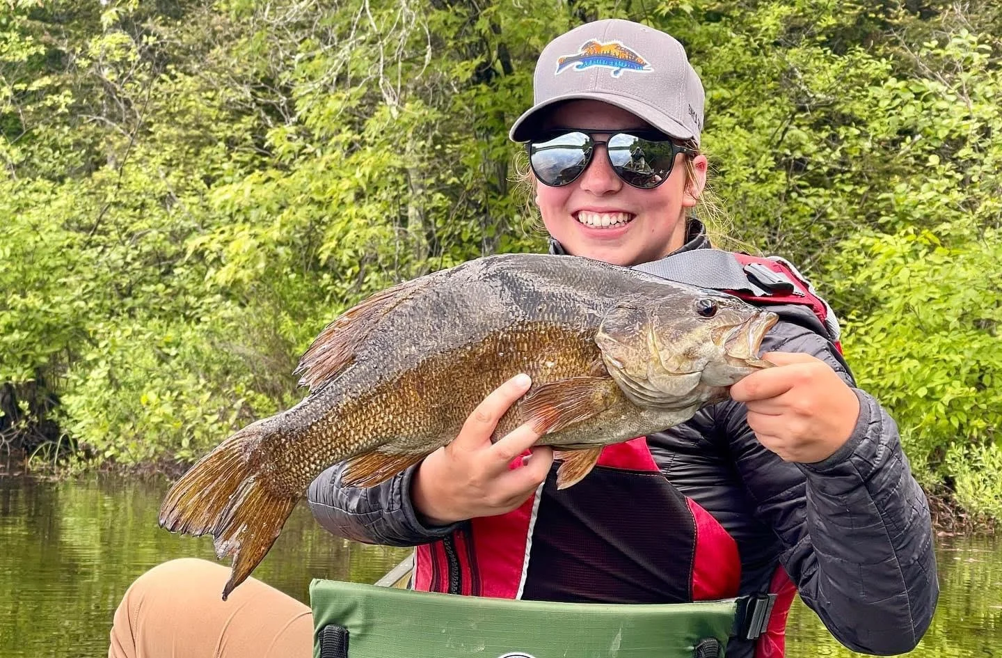 Angler holds smallmouth bass from canoe with Cast Outdoors Guide Ely MN, BWCA area, June 25 2024. Arrowhead Outdoors Ely MN fishing report with premium tackle, hunting gear & camping supplies available.
