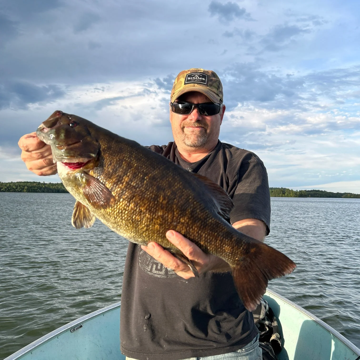 Angler holds chunky smallmouth bass in boat at sunset on Ely MN lake, BWCA area, September 19 2023. Arrowhead Outdoors Ely MN fishing report with premium tackle, hunting gear & camping supplies.