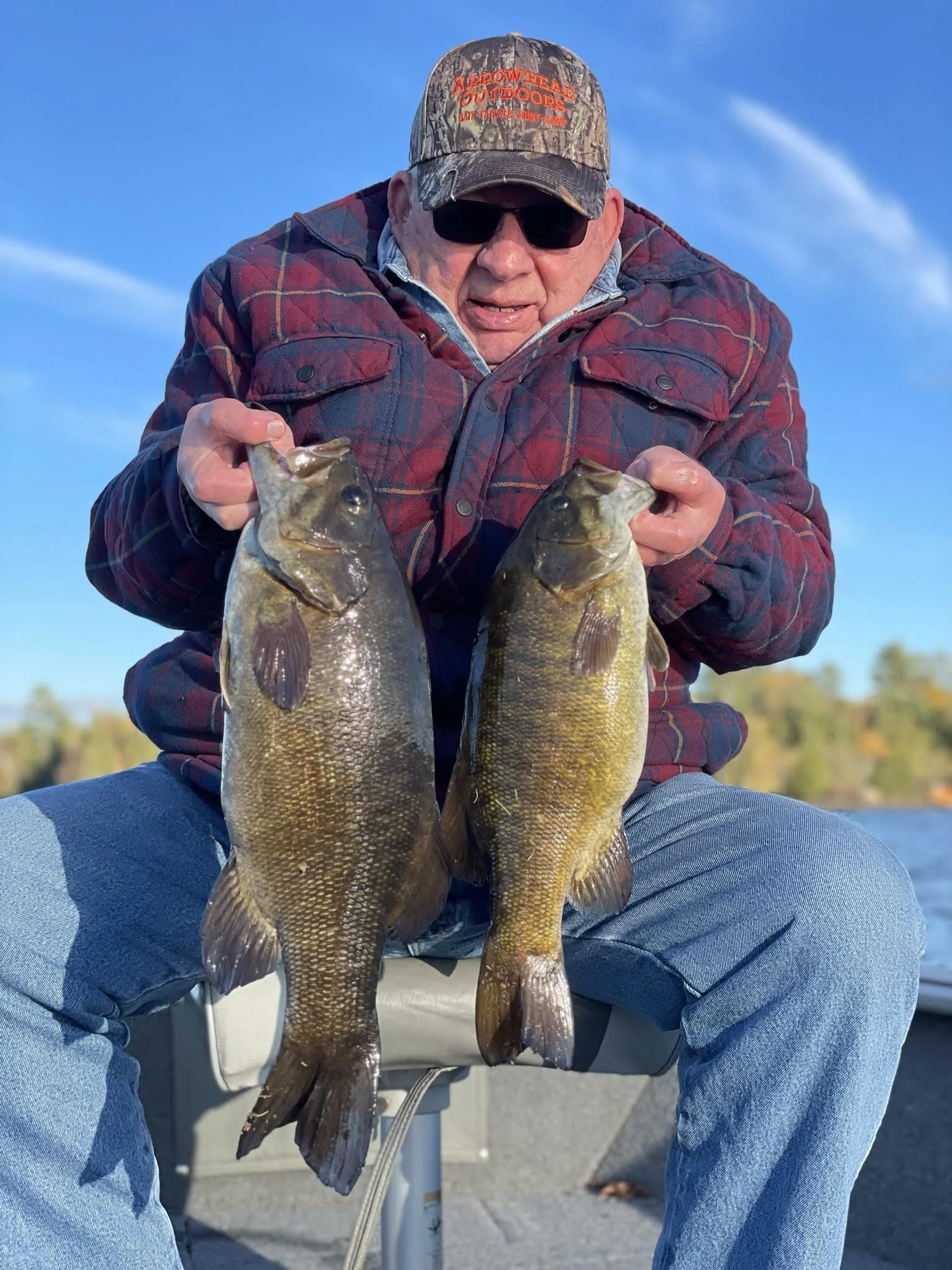 Angler holds two chunky smallmouth bass in boat under fall sky on Ely MN lake, BWCA area, October 10 2023. Arrowhead Outdoors Ely MN fishing report with premium tackle, hunting gear & camping supplies.