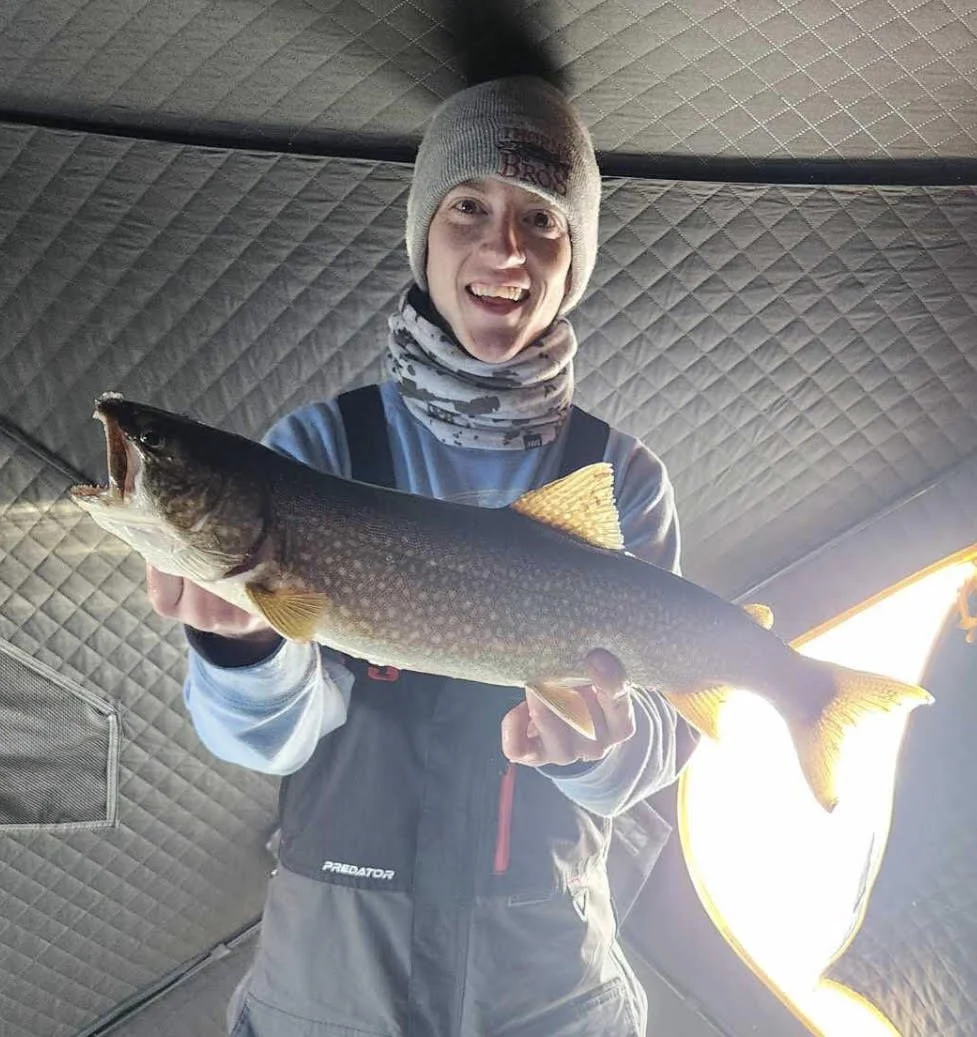 Angler holds lake trout caught on Laker Tackle tube inside heated ice shelter on Ely MN ice, BWCA area, February 27 2024. Arrowhead Outdoors Ely MN winter fishing report with ice house rentals, premium tackle, hunting gear & camping supplies.
