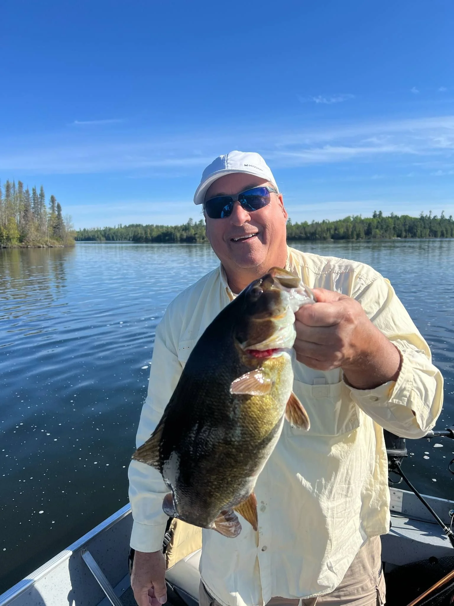 Man holding smallmouth bass in boat Ely MN BWCA from Arrowhead Outdoors May 31 2022 fishing report shallow bays boulders rocky points jerk baits tubes sunny open water pine shores Northwoods scene walleye solid pike excellent stream trout active