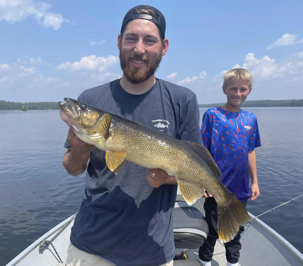 Ely MN BWCA walleye catch in Arrowhead Outdoors fishing report July 4 2023 – angler and boy holding golden walleye on boat sunny lake