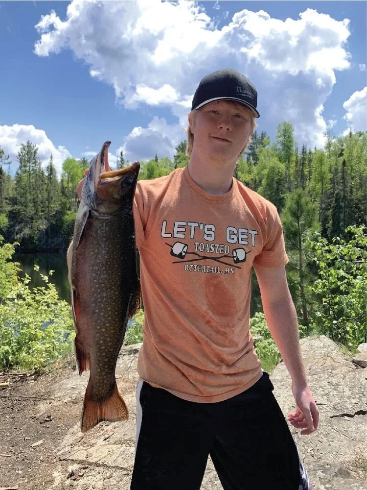 Ely MN BWCA brook trout open water catch June 8 2021, young angler holding speckled brookie by rocky shore under sunny sky, Arrowhead Outdoors report