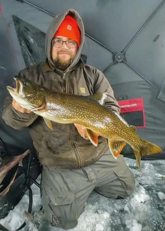 Angler holds lake trout inside heated ice shelter on Ely MN ice, BWCA area, January 16 2024. Arrowhead Outdoors Ely MN winter fishing report with ice house rentals, premium tackle, hunting gear & camping supplies.