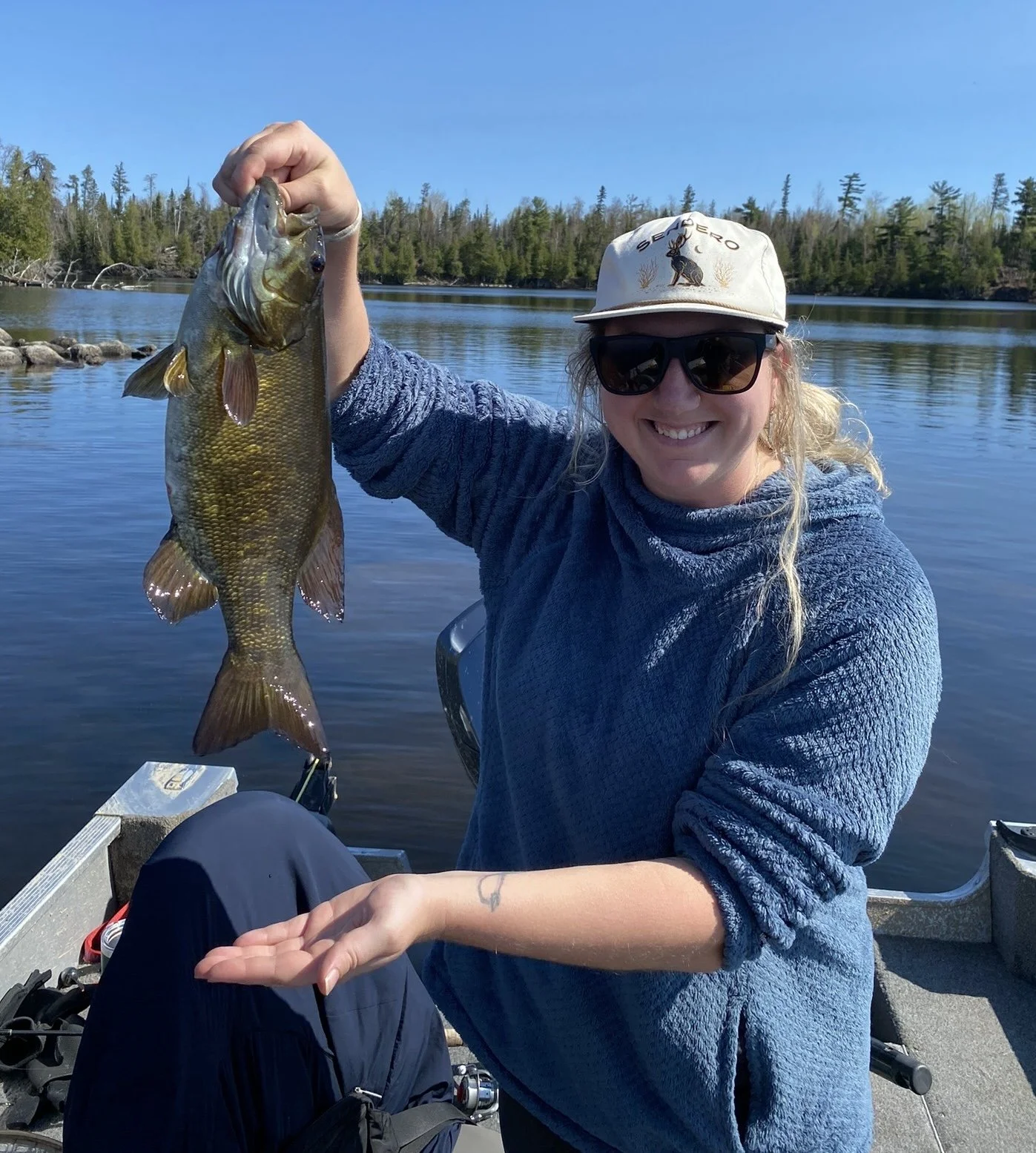 Angler holds smallmouth bass caught on Whopper Plopper in boat Ely MN, BWCA area, June 4 2024. Arrowhead Outdoors Ely MN fishing report with premium tackle, hunting gear & camping supplies available.