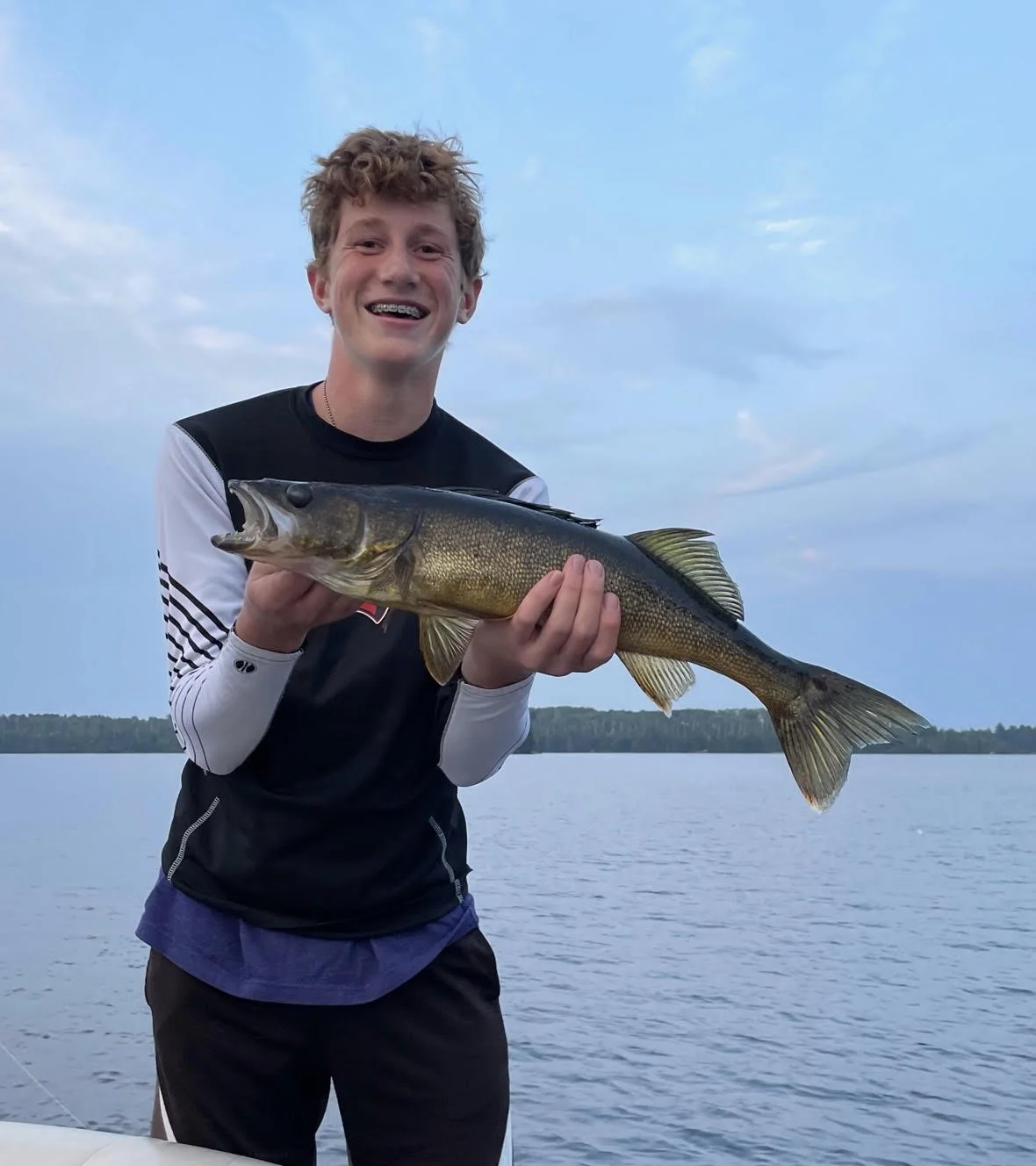 Ely MN BWCA walleye catch in Arrowhead Outdoors fishing report August 15 2023 – young angler holding golden walleye on boat calm lake