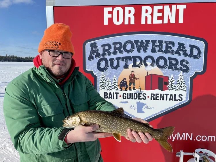 Ely MN BWCA lake trout catch in Arrowhead Outdoors fishing report January 17 2023 – angler holding spotted laker by red ice house rental sign Ely MN