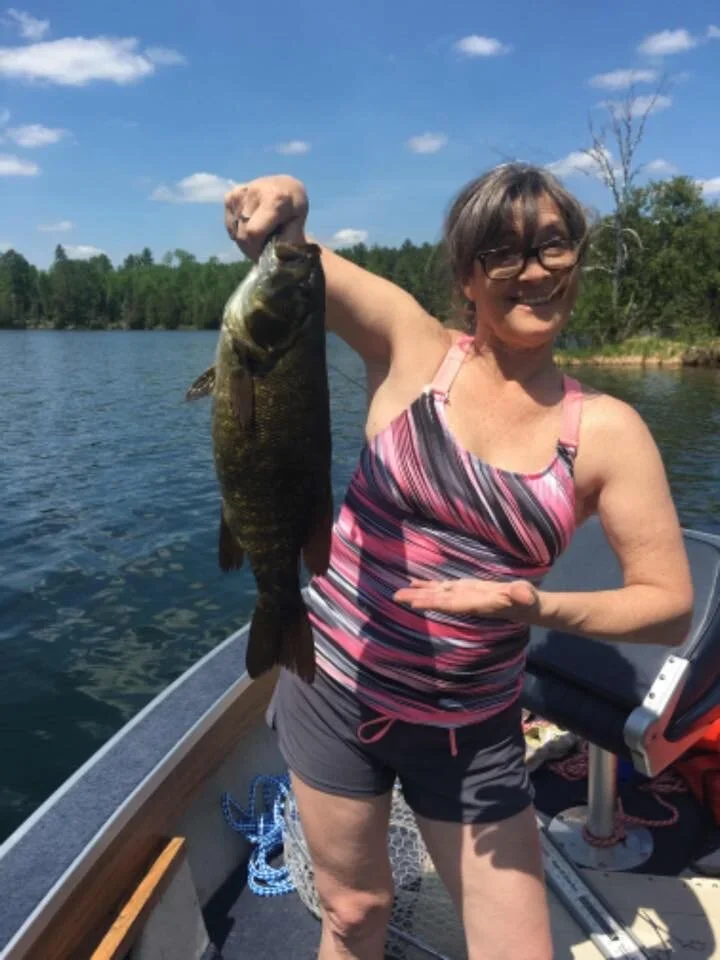 Ely MN BWCA smallmouth bass open water catch July 27 2021, woman holding dark bronze smallie on sunny boat, Arrowhead Outdoors report