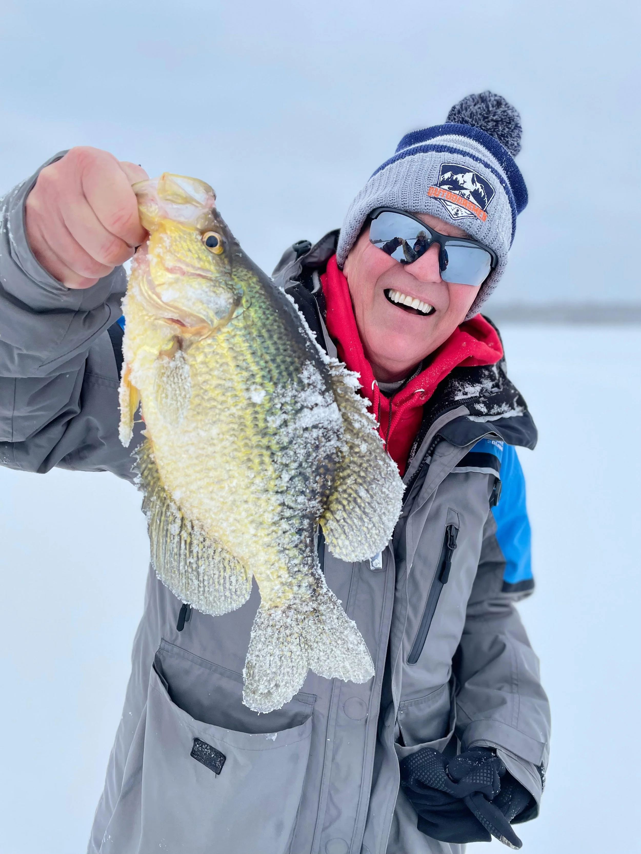 Ely MN BWCA crappie catch in Arrowhead Outdoors fishing report January 31 2023 – angler smiling wide holding golden crappie on snowy ice BWCA lake