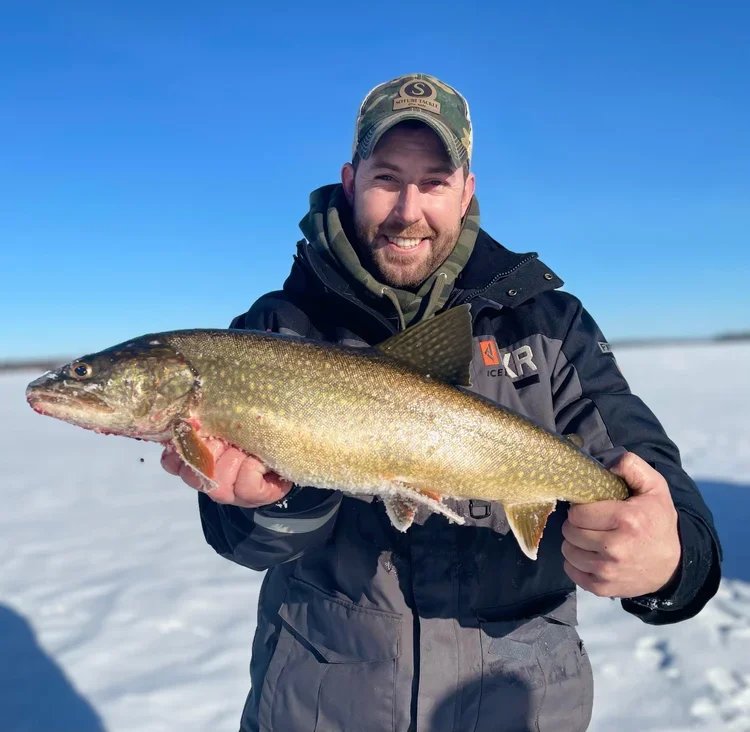 Ely MN BWCA lake trout catch in Arrowhead Outdoors fishing report January 10 2023 – angler smiling on ice holding spotted laker bright blue sky